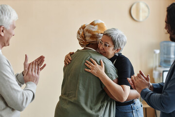 Diverse group of elderly people applauding and embracing celebrating in support group