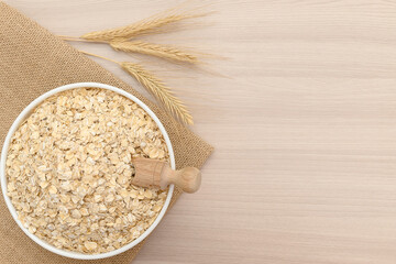 Oatmeal flakes in a white bowl with ears of wheat. Scoop wooden.