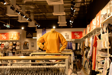 Clothing store interior with red banners and discounts. Mannequin in the window in an orange hoodie. Black Friday, sale, shopping, discounts, a lot of clothes, new clothes, second hand.