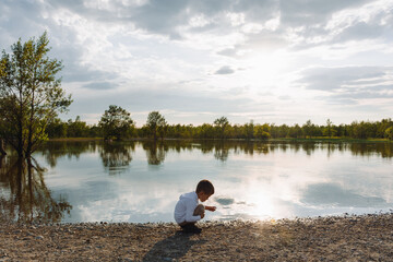 Fototapeta na wymiar Little boy playing by a pond in a park at sunset