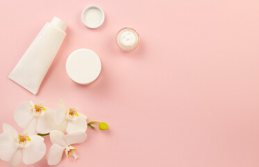 Obraz na płótnie Canvas White jars for cosmetic products and orchid flowers on a pink background. Mockup for cosmetic products with place for text.