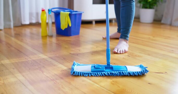 Woman in casual clothes washing a wooden floor with a damp microfiber mop
