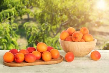 Bowl with ripe apricots and wooden board on table outdoors