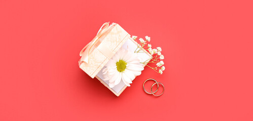 Box with flowers and wedding rings on red background, top view