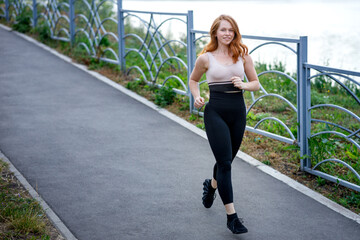 a red-haired girl running along the sidewalk along the river on a summer evening