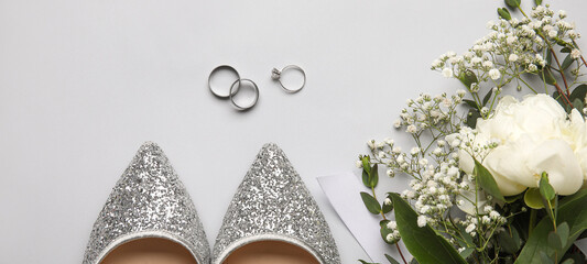 Wedding and engagement rings with female shoes and flowers on light background