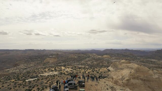 Aerial-Pull back-unidentifiable off road vehicles and riders stopped at a scenic overlook on a narrow desert point point of the canyon rim - birds flying through the scene