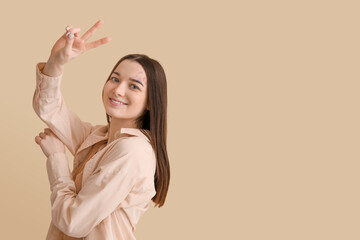 Young woman showing victory gesture on beige background