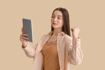 Young woman with tablet computer pointing at something on beige background