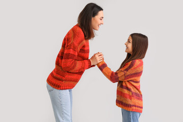 Little girl and her mother in warm sweaters holding hands on grey background