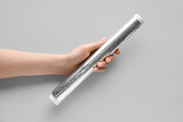 Female hand with aluminium foil roll on grey background