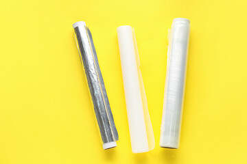Rolls of aluminium foil, food film and baking paper on yellow background