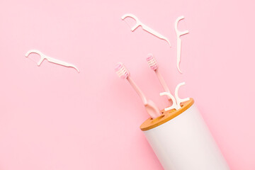Overturned toothbrush holder and floss toothpicks on pink background - obrazy, fototapety, plakaty