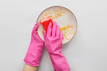 Female hands in rubber gloves washing dirty plate with sponge on grey background