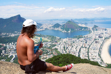 back view Latin American tourist sitting and looking a beautiful panoramic aerial view of Rio de Janeiro	 - Powered by Adobe
