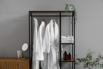 Fototapeta na wymiar Shelving unit with bathrobes and bath accessories in interior of light room