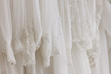 Beautiful white wedding dresses are hanging on hangers in the bridal salon. Background for the design of a wedding clothing store.