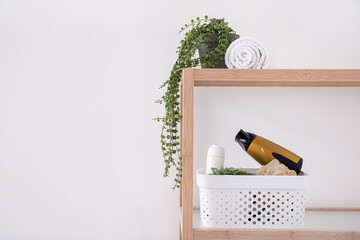 Shelving unit with bath accessories and houseplant near light wall