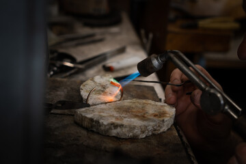 Fototapeta na wymiar Jeweler soldering on work bench a gold ring bracelet with flame from welding torch in an authentic jewelry workshop