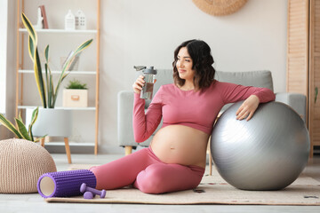 Sporty pregnant woman with bottle of water and fitball at home