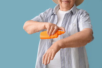 Senior woman with sunscreen cream on blue background, closeup