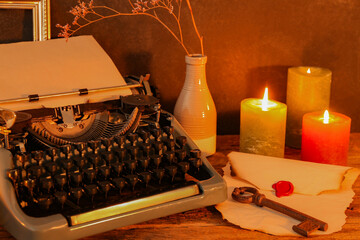 Vintage typewriter, burning candles, old key and envelope with wax seal on wooden table