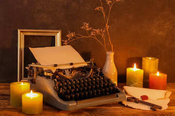 Vintage typewriter, burning candles, old key and envelope with wax seal on wooden table