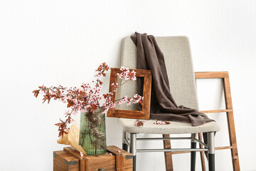 Vase with blooming tree branches on wooden drawer and chair near white wall