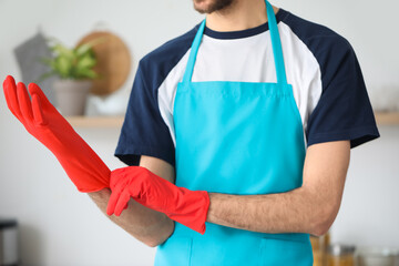 Young man putting rubber gloves in kitchen, closeup