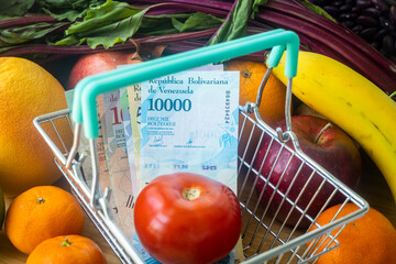 Venezuelan money in a shopping cart, Vegetables and fruits, Concept, Growing food prices in Venezuela - obrazy, fototapety, plakaty