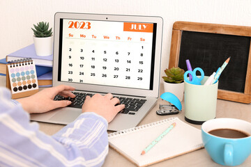 Fototapeta na wymiar Woman using modern laptop with calendar at workplace
