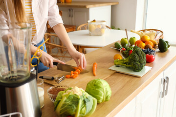 Young woman cutting carrot in kitchen, closeup