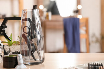 Glass with different hairdressing tools on table in beauty salon