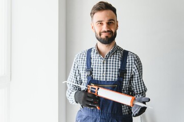 Contractor hand holding glue gun with silicone to repair tile and window. Installation or...