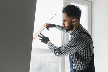 Contractor hand holding glue gun with silicone to repair tile and window. Installation or renovation interior concept. - obrazy, fototapety, plakaty