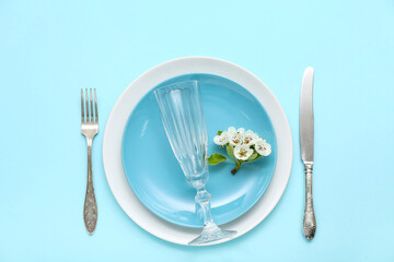 Beautiful table setting with empty glass and blooming tree branch on turquoise background