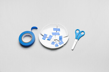 Broken plate with adhesive tape and scissors on light background