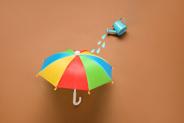 Creative composition with mini watering can and umbrella on brown background