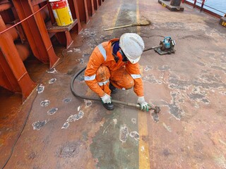 A ship crew or seaman is chipping or derusting main deck onboard a cargo ship or bulk carrier...