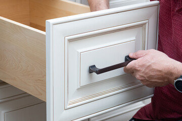 the worker sets a new handle on the white cabinet with a screwdriver