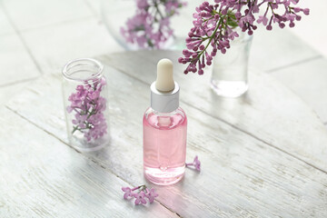Obraz na płótnie Canvas Bottles of cosmetic oil with beautiful lilac flowers on white table