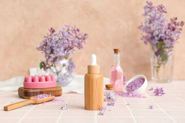 Bottles of cosmetic oil with beautiful lilac flowers and sea salt on pink tile table