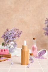 Obraz na płótnie Canvas Bottles of cosmetic oil with beautiful lilac flowers and sea salt on pink tile table