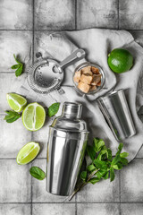 Shaker, strainer and ingredients for preparing mojito on black tile background