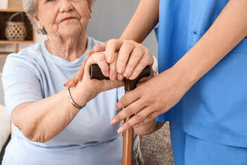 Senior woman with walking stick and female caregiver at home, closeup