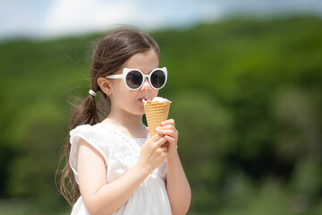 Beautiful little girl in sunglasses and white dress eating an ice cream. High quality photo