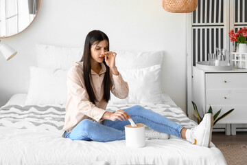 Allergic young woman sneezing in bedroom