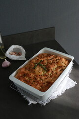 Italian garlic rosemary focaccia bread in white baking pan on grey table with sunlight 