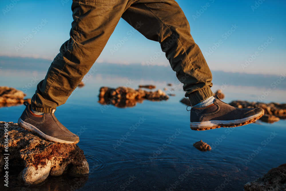 Sticker Boy walking on stones in the lake, close-up focus on boots