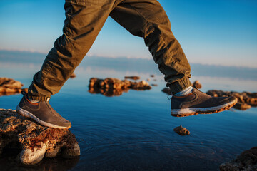 Boy walking on stones in the lake, close-up focus on boots